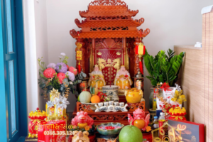 Ban thờ Thần Tài Thổ Địa mái chùa bằng gỗ đặt sát nền, bày hoa tươi, ngũ quả và bộ đồ thờ